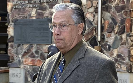 Tom Crosby seen from the chest up in a suit in front of a stone wall.