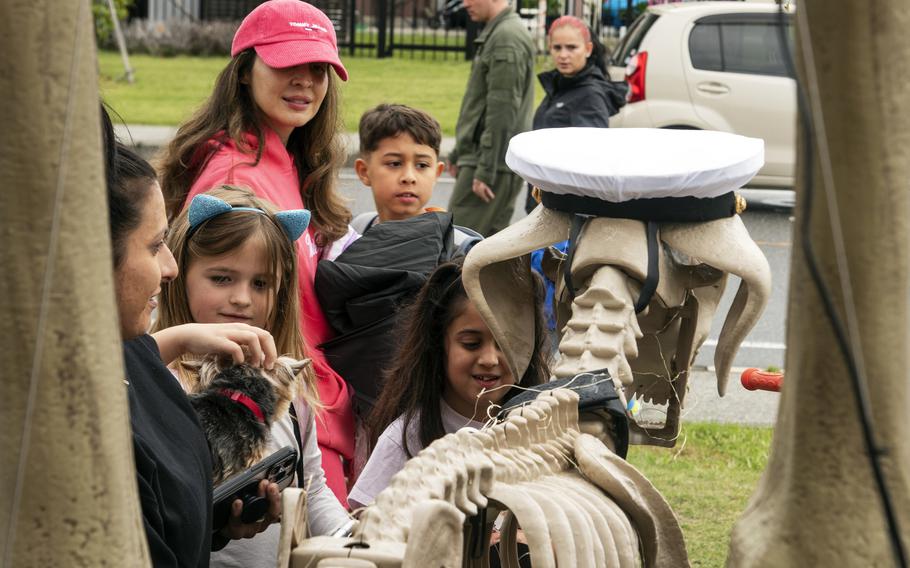 A group of children gather around a Halloween decoration of a skeletal dog.