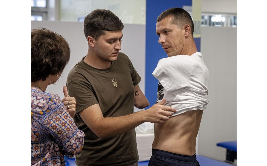 Ilia Mykhalchuk is helped into his shirt by fellow wounded Ukrainian veteran Denys Stratiishuk after being fitted for prosthetics. 