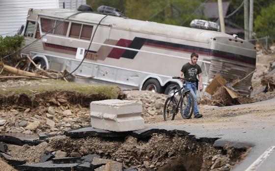 A man walks with a bicycle along a damaged road past debris from Hurricane Helene.