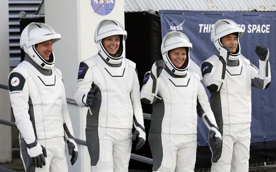 Four astronauts in space suits and helmets flash smiles.