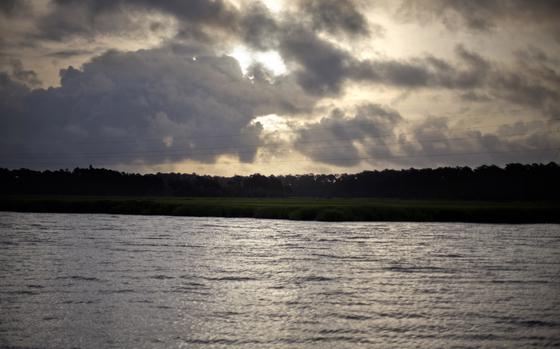 Sunlight filters through gray clouds over a gray body of water.