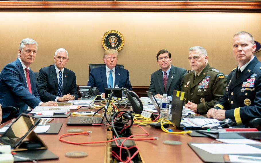 The U.S. president and his advisors sit at a table with laptops and wires strewn over it.