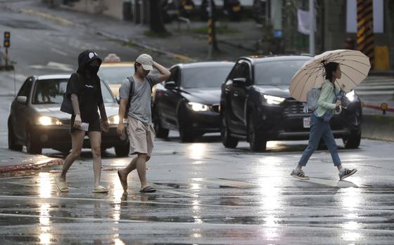 Pedestrians cross a street in the rain.