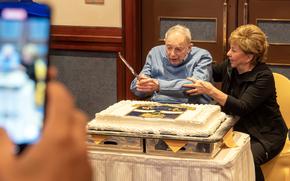 World War II veteran Norman Jay Green prepares to cut a large cake during his 100th birthday celebration at the New Sanno Hotel in Tokyo, Nov. 22, 2024. The cake features the insignia and motto of the 326th Glider Infantry Regiment: “Aspera Juvant,” Latin for “Difficult Delight.” 