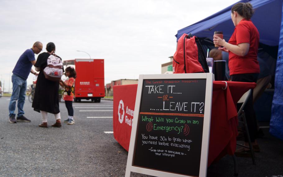 A sign at a booth reads “Take it or leave it? What will you grab in an emergency?” Participants in the Great ShakeOut event talk to each other in the background. 