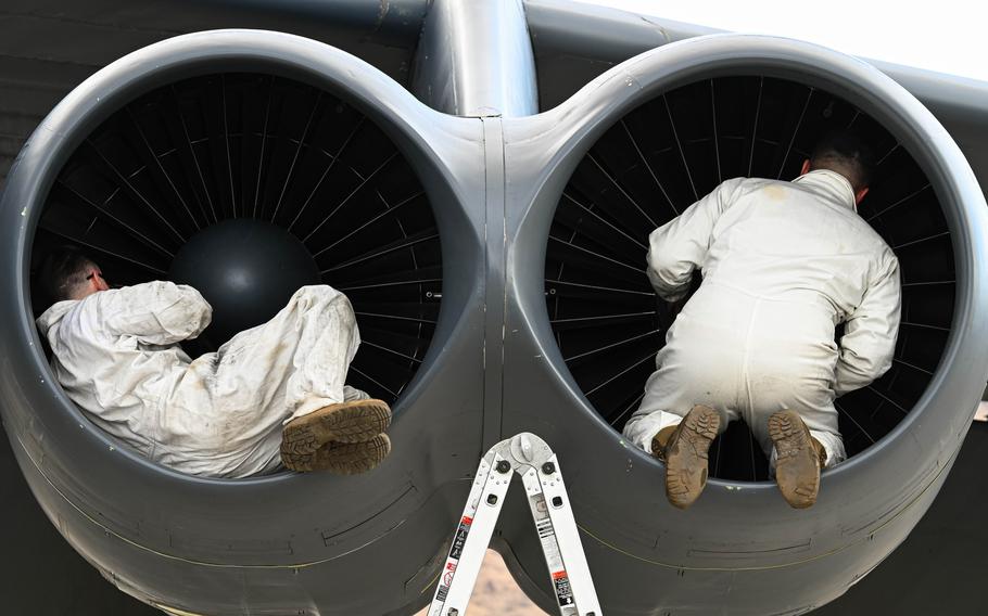 Two airmen perform maintenance on the engine of an aircraft