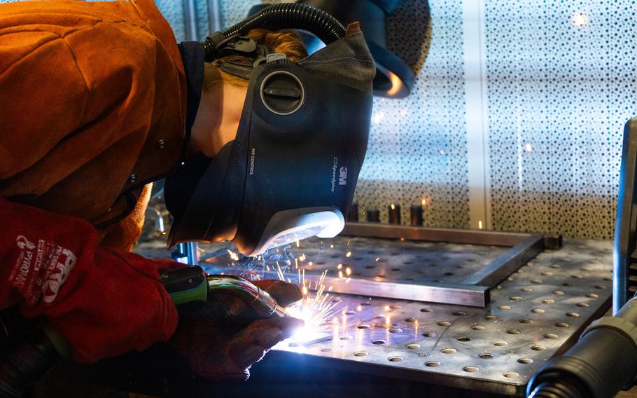 A student with a mask works with a welding tool.