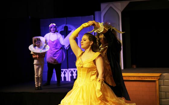 Belle, wearing a yellow ballgown, dances with the Beast as Mrs. Potts the enchanted teapot and Chip the teacup look on. 