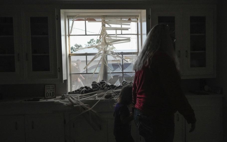 A woman and a young girl walk past a broken window inside a house.