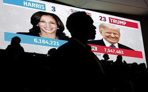 A man is silhouetted in front of a video screen showing election results between Kamala Harris and Donald Trump.