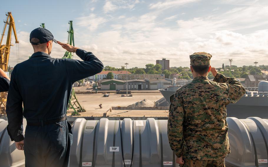 A sailor and a Marine salute as the USS New York enters port in Lithuania.