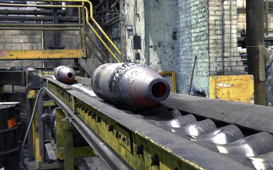 Scranton Army Ammunition Plant’s nosing process is depicted as ammunition parts move on a conveyor to the heat-treating process. Nosing is the process where the open end of the cylindrical parts are formed into the roundly tapered ogive.  The parts are glowing red from prior heating before the forming process. 