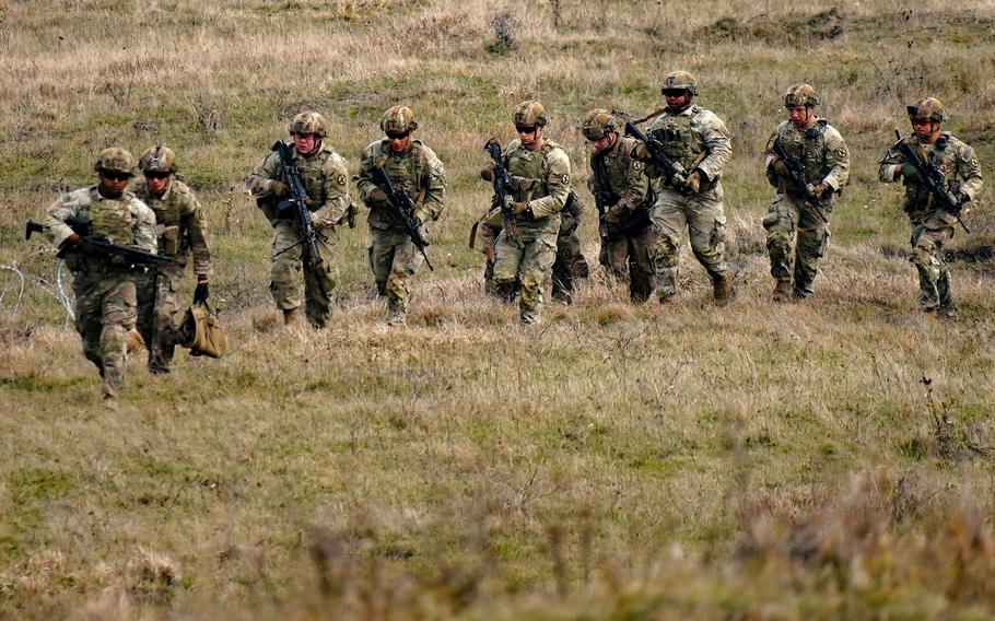 Nine soldiers in uniform walk through a field. 