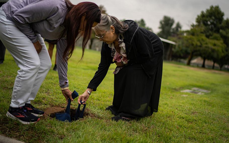 Rachel Twitchell-Justiss, left, and Martha Sara Jack, both cousins of Mary Sara's, lower into the ground a suede bag containing a wooden box holding her brain. 