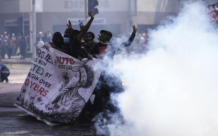 Protesters hide behind a banner as police fire teargas at them during a protest over proposed tax hikes in a finance bill in downtown Nairobi, Kenya Tuesday, June 25, 2024. 