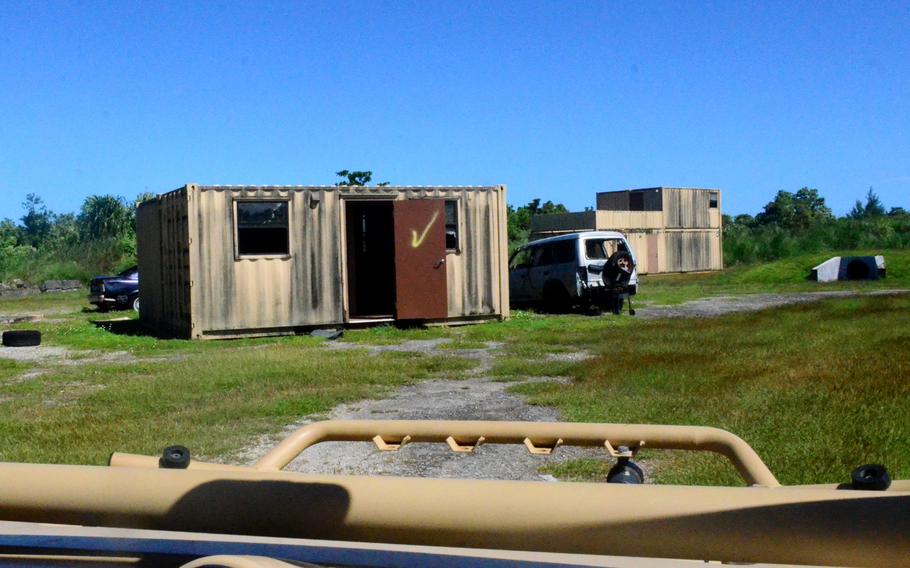 Cars in a field are parked next to shipping container buildings as a part of a training course.