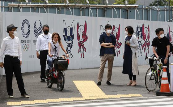 People stand by posters to promote the Tokyo Olympic Games scheduled to start in the summer of 2021, in Tokyo, Monday, May 24, 2021. (AP Photo/Koji Sasahara)