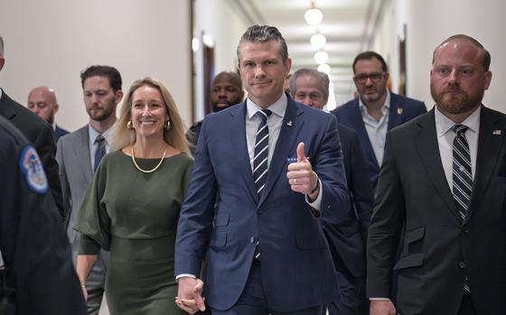 Pete Hegseth gives a thumbs-up as he walks with his wife and others at the Capitol.