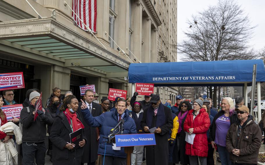 A group of people at a podium and holding signs outside a building.