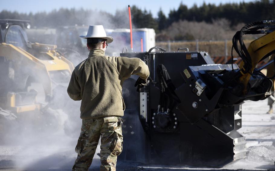 An airman acts as a ground guide while wheel saws are used to remove a patch of damaged concrete on a runway at Yokota Air Base.