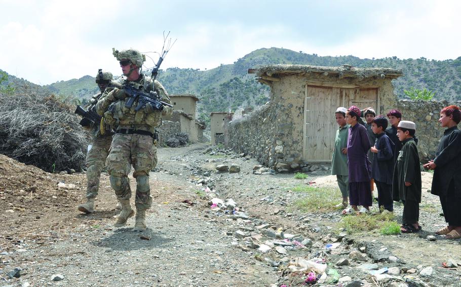 Children gather to watch Sgt. Joshua Sutherland, front, and Pfc. Alex Bolden enter a village