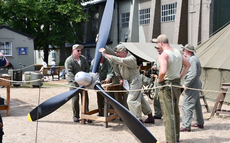 Reenactors portraying WWII-era U.S. Army Air Forces aviation armorers and mechanics work together to place a propeller for display at the Duxford Air Show.