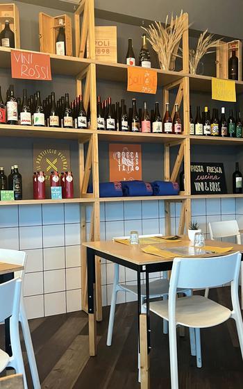 A wooden table is underneath shelves showing olive oil and other products for sale.