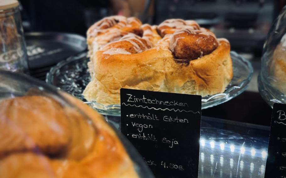 A vegan cinnamon roll lies on a black plate. 