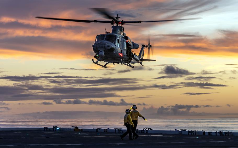 Two air traffic controlles look up at a helicopter as it lands on the deck of a ship.