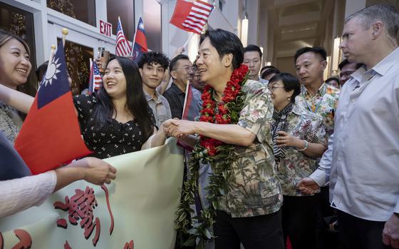 A man wearing a floral shirt and lei greets a line of people holding flags and signs.