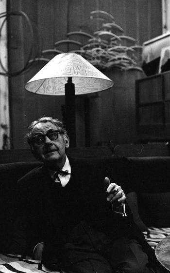 Artist Man Ray, photographed in his Paris studio. Hanging behind him his work “Obstruction.”