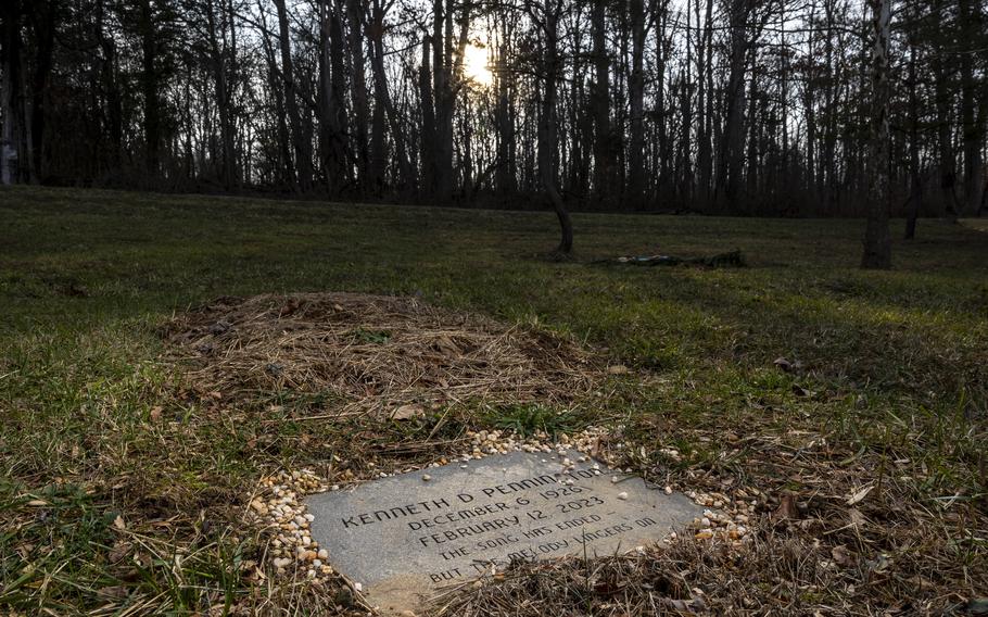 A flat engraved stone noting the gravesite of a WWII veteran is seen before a patch of ground.