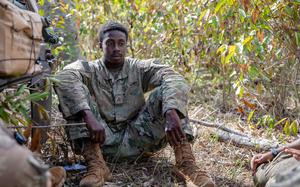 An Army soldier in uniform sits on the ground.