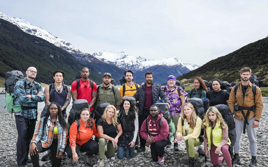 A group of people in hiking gear stand in front of a mountain range.