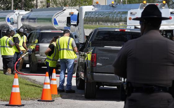 A truck and an SUV are filled with gas by workers wearing safety vests.