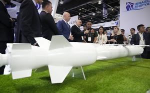 People in business attire look at a white missile displayed on green turf.