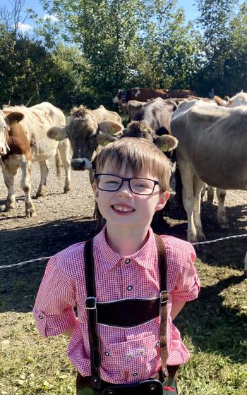 Small boy dressed in tradional Bavarian clothing standing in front of cows