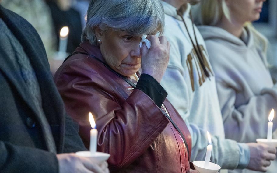 A woman holding a candle wipes her eye.