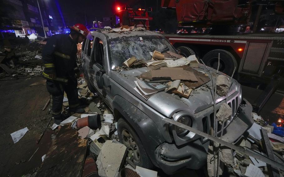 A firefighter inspects a damaged car covered with debris from an airstrike.