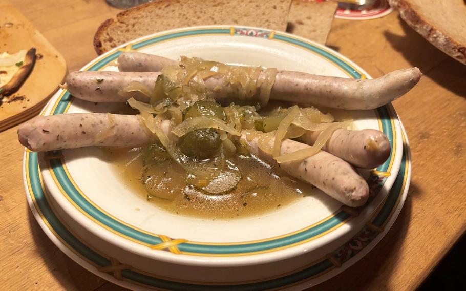 Three bratwurst on a white plate topped with shaved onions and pickles.