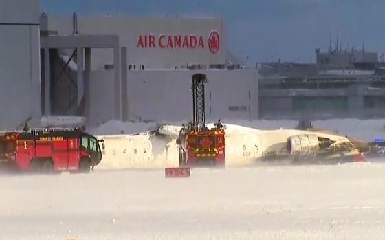 Emergency vehicles next to a Delta Airlines plane, flipped over on the tarmac.