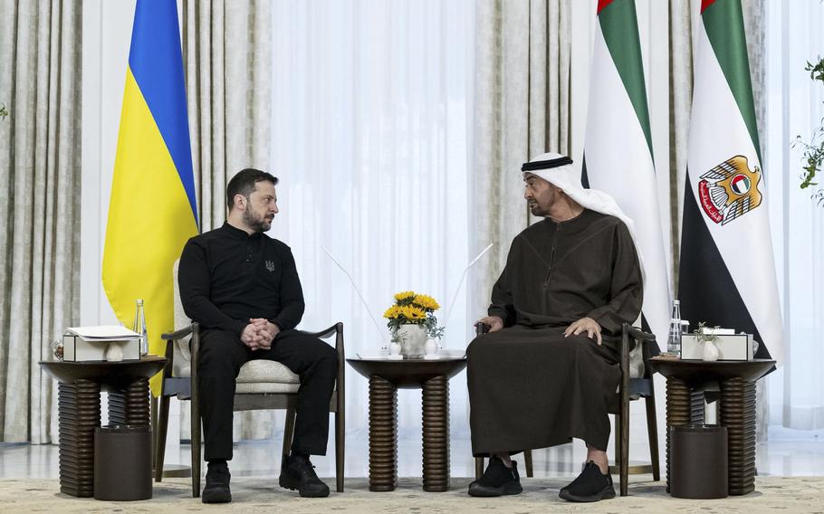 Volodomyr Zelenskyy and Mohammed bin Zayed Al Nahyan sit next to each other, with their respective flags behind them.