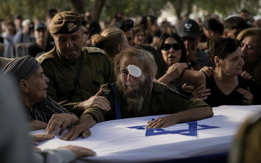 A man with an eyepatch mourns over a coffin draped with an Israeli flag.