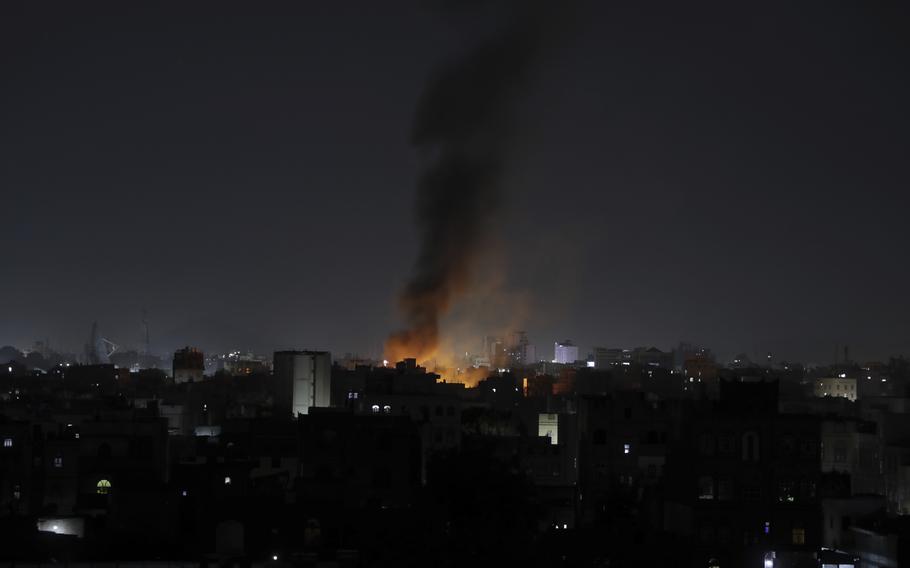 Illuminated smoke rises over a dark city skyline after a nighttime airstrike.