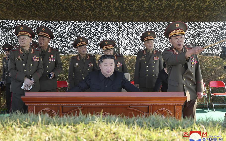 North Korean leader Kim Jong Un sits at a desk outside, flanked by a group of military officials.