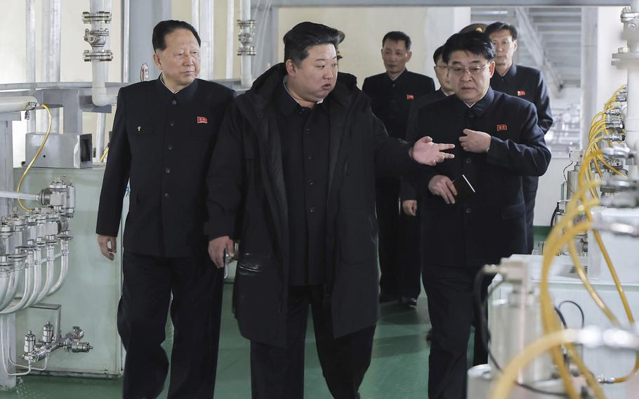 Kim Jong Un, dressed in black with a black coat, speaks with North Korean officials as they walk along a corridor in a nuclear facility.