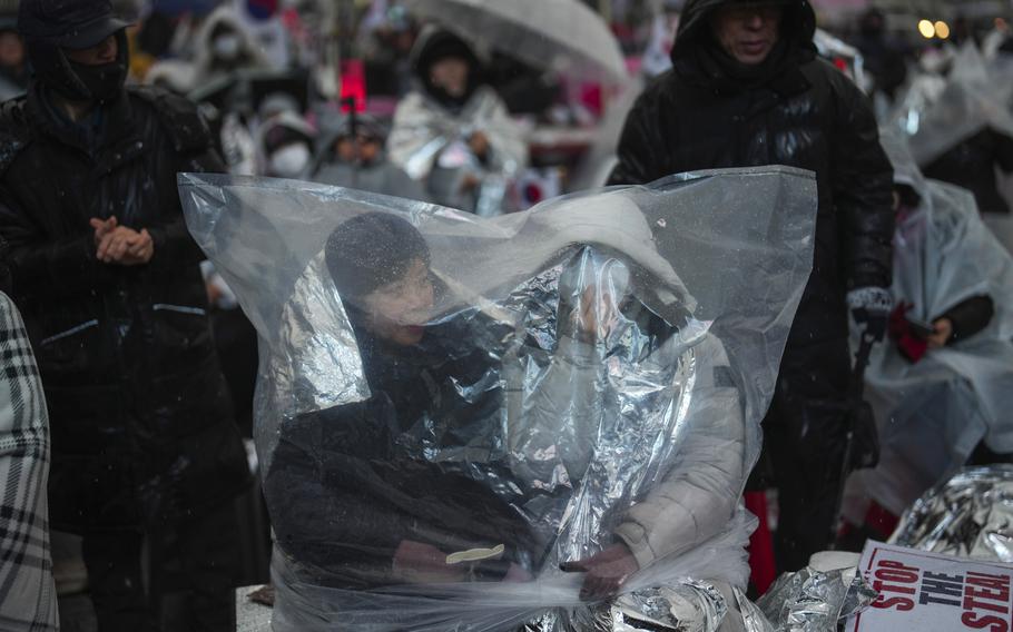 People sit outside under a plastic sheet in the rain as a part of a rally.