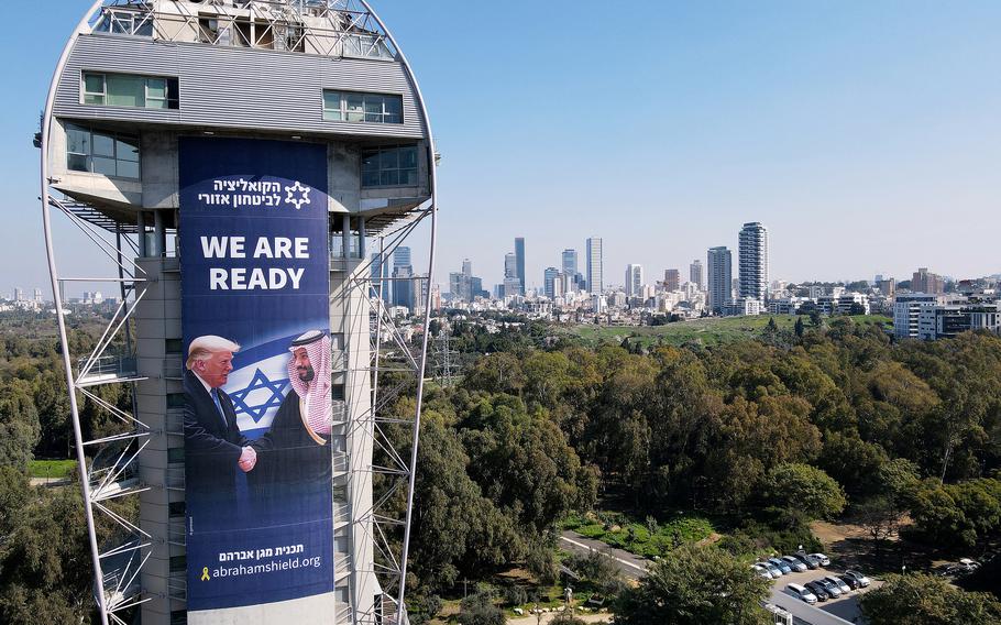 A large banner poster reads “We are ready” with a photo of President Trump shaking hands with the leader of Saudi Arabia, set against the Israeli flag.