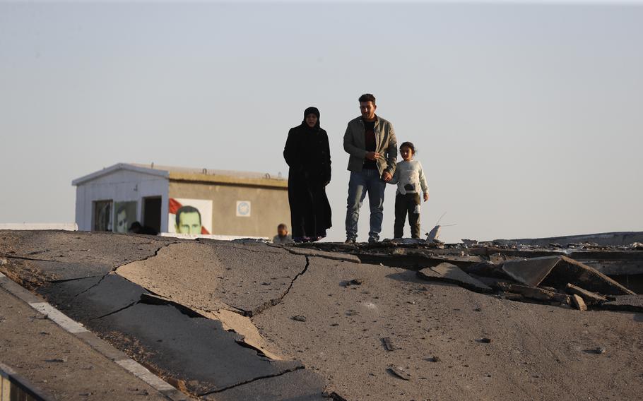 A woman, man and child look at a destroyed concrete bridge.